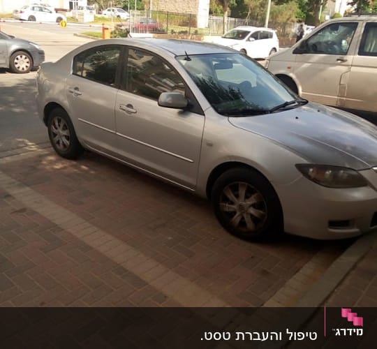 מכונית כסופה חונה על מדרכה ליד כביש